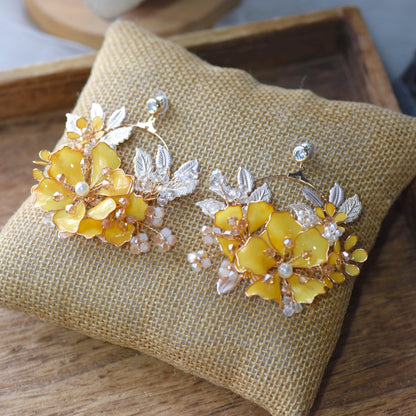 Helios yellow and golden resin floral earrings laid flat on a jute cushion
