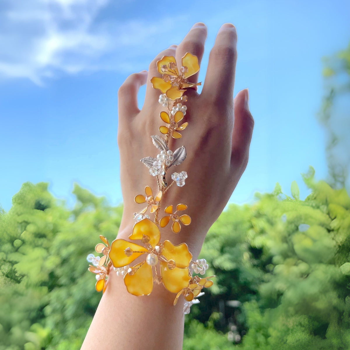 Hand raised against the sky wearing the Helios yellow and golden resin floral hand harness
