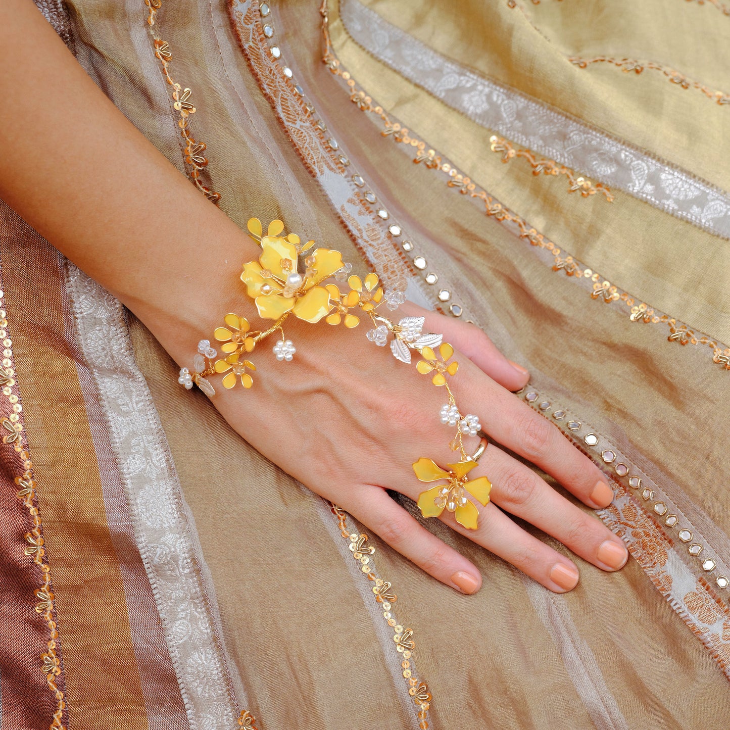 Helios yellow resin floral hand harness worn on the hand against a gold embroidered outfit
