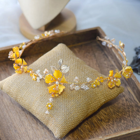 Helios yellow resin floral head harness with golden and ivory accents laid on a jute cushion
