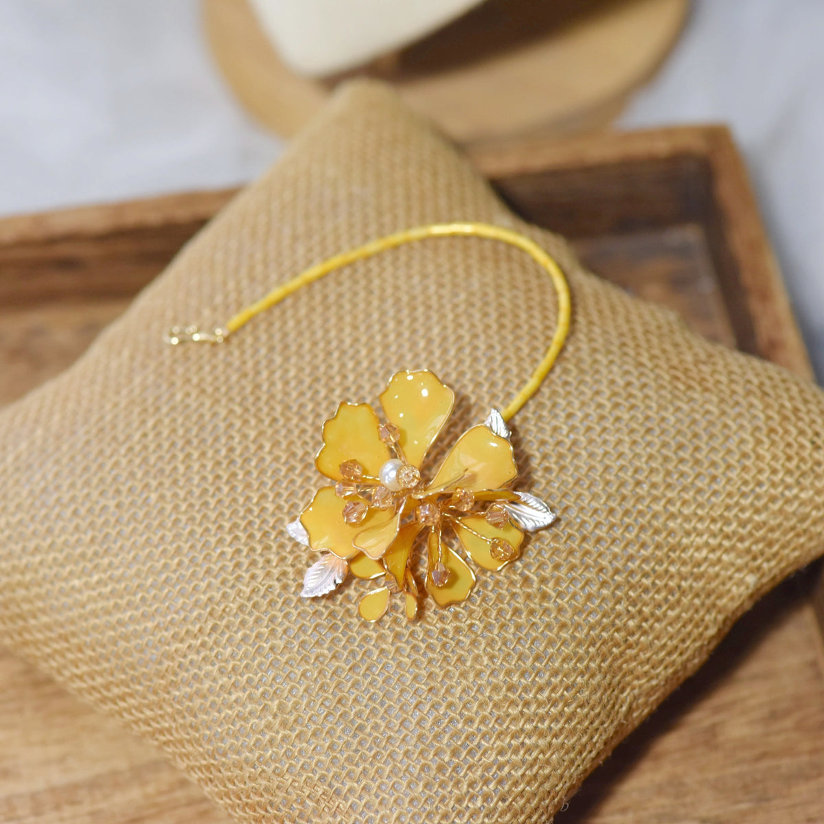 Helios yellow resin floral maang tika with golden chain laid on a jute cushion
