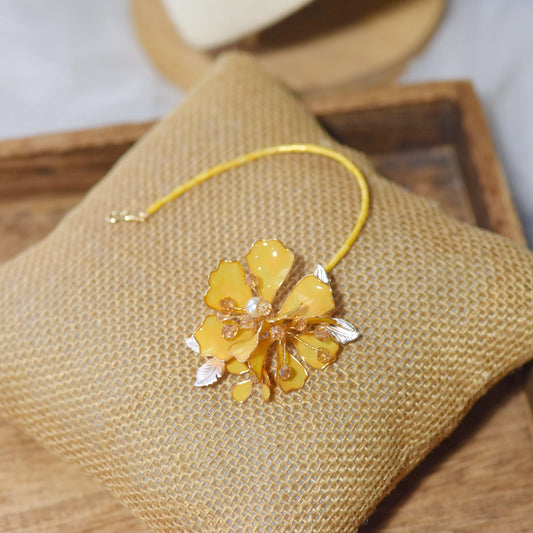 Helios yellow resin floral maang tika with golden chain laid on a jute cushion
