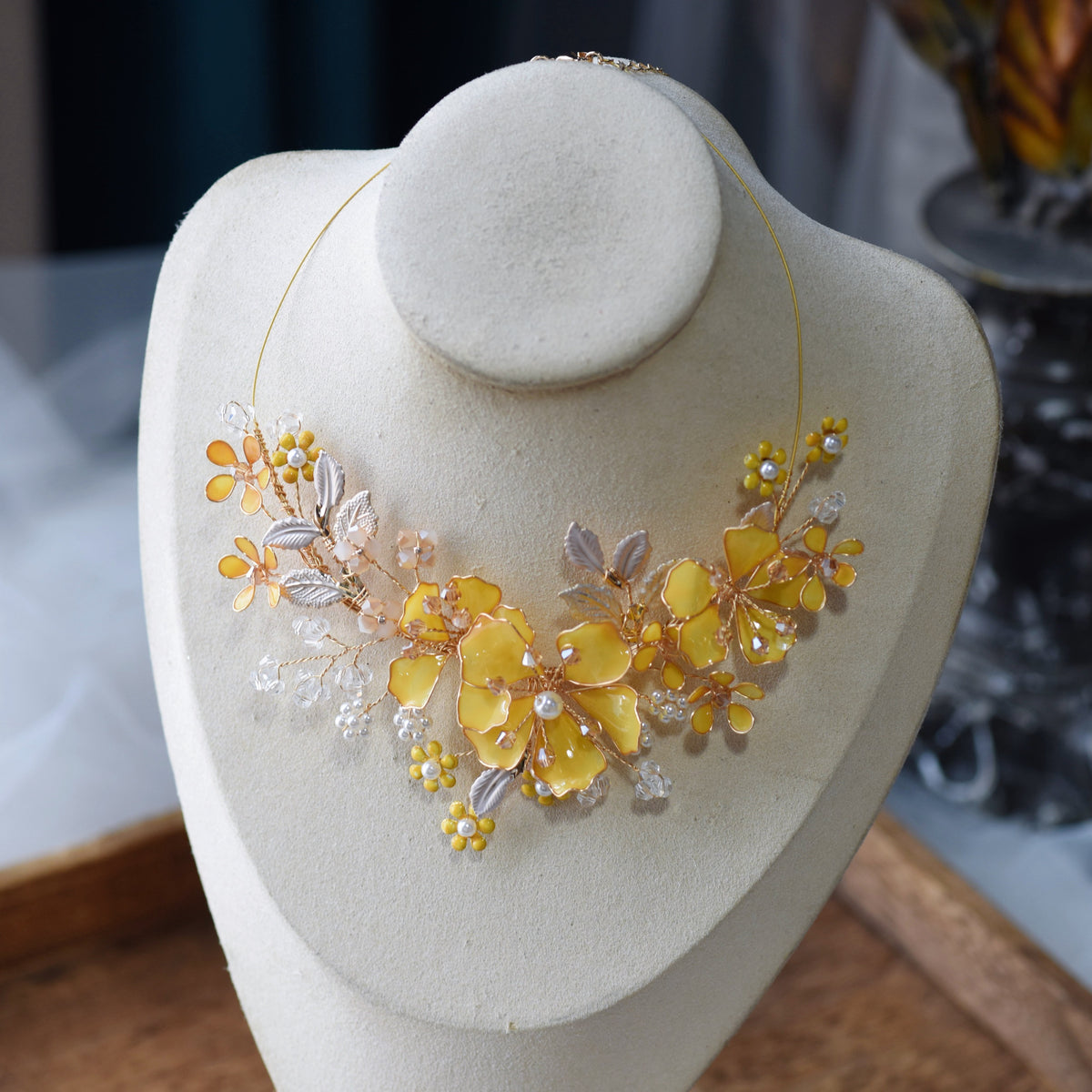 Helios yellow and golden resin floral statement necklace displayed on a stand showing the asymmetric bloom cluster
