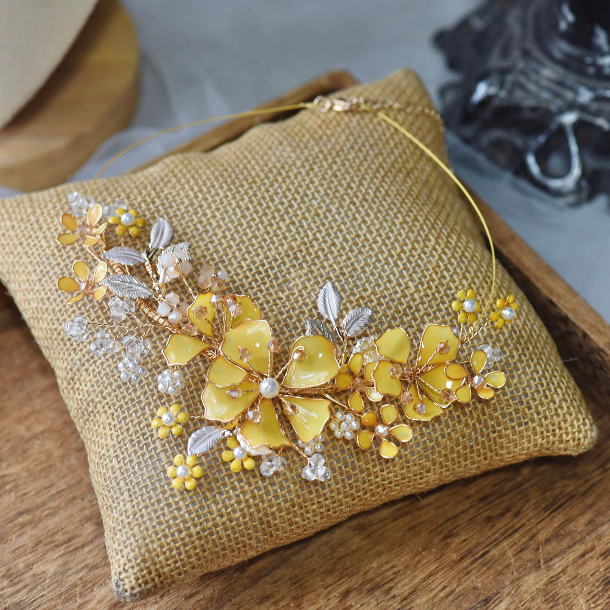 Helios yellow resin floral necklace with golden and ivory accents laid on a jute cushion
