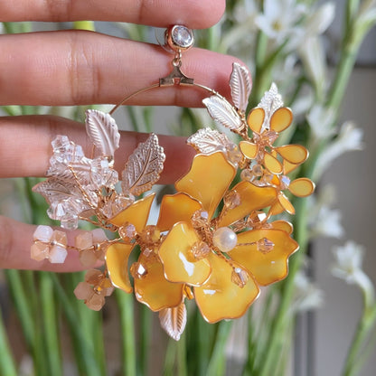 Close view of Helios yellow resin floral earring held in hand showing petal detail and golden shades
