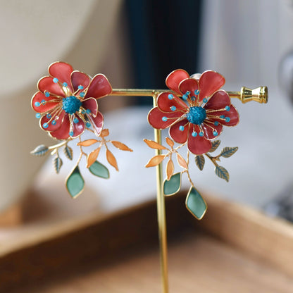 Isariah red resin floral stud earrings with blue centres and green leaves on a display stand
