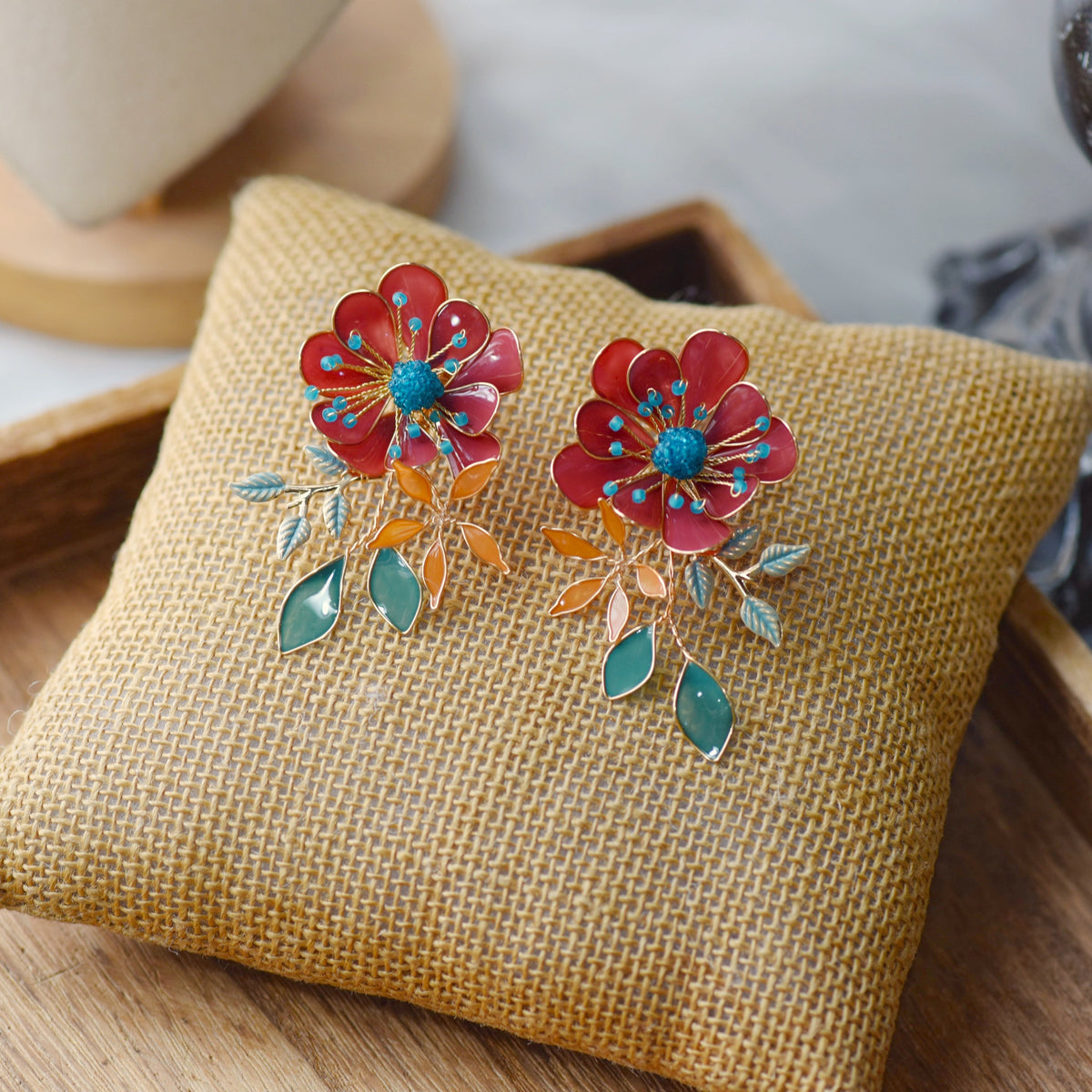 Isariah red and green resin floral stud earrings on a jute cushion
