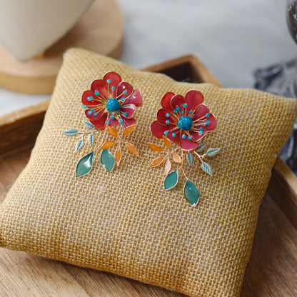 Isariah red and green resin floral stud earrings on a jute cushion
