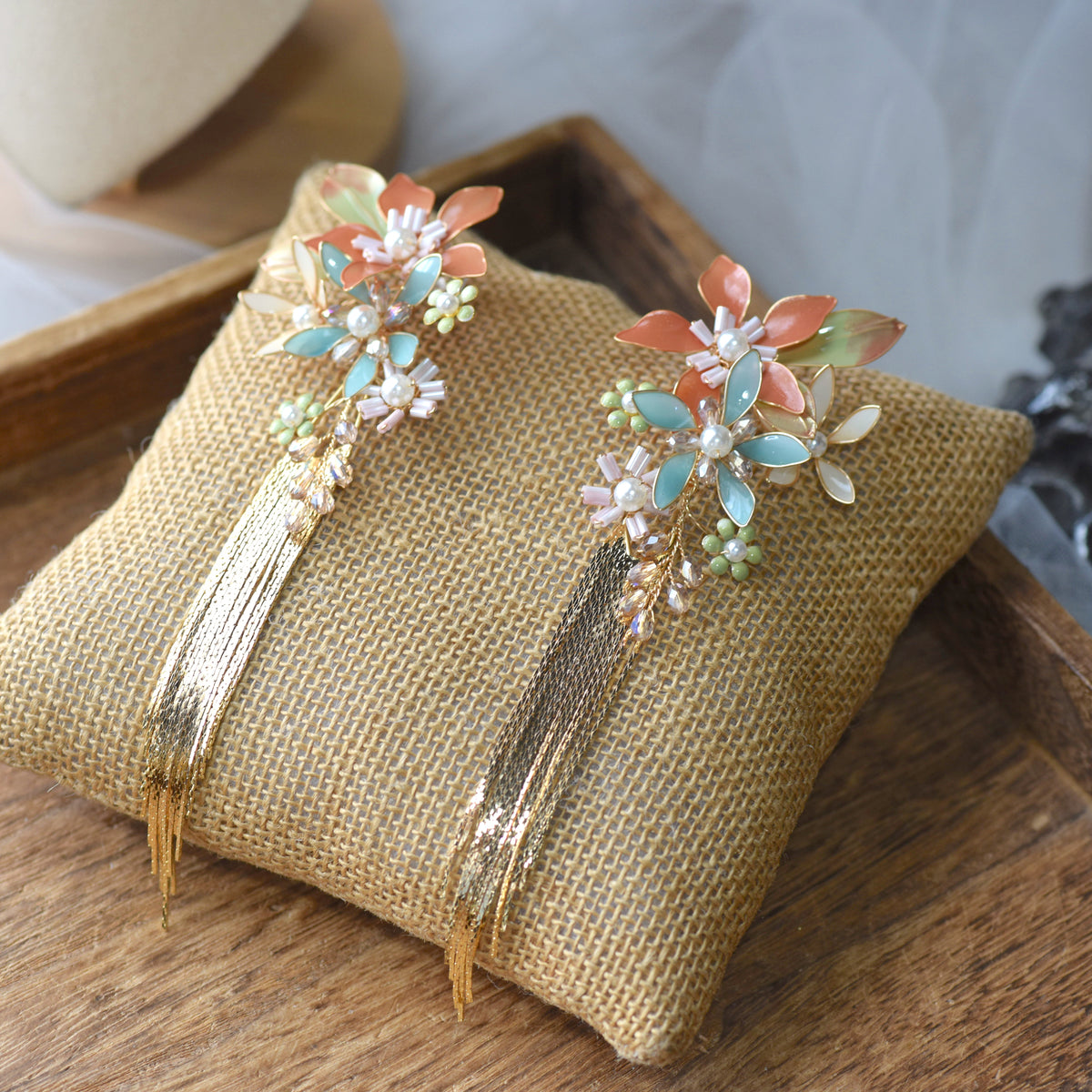 Jeanne coral mint and blue resin floral earrings with golden tassels on a jute cushion
