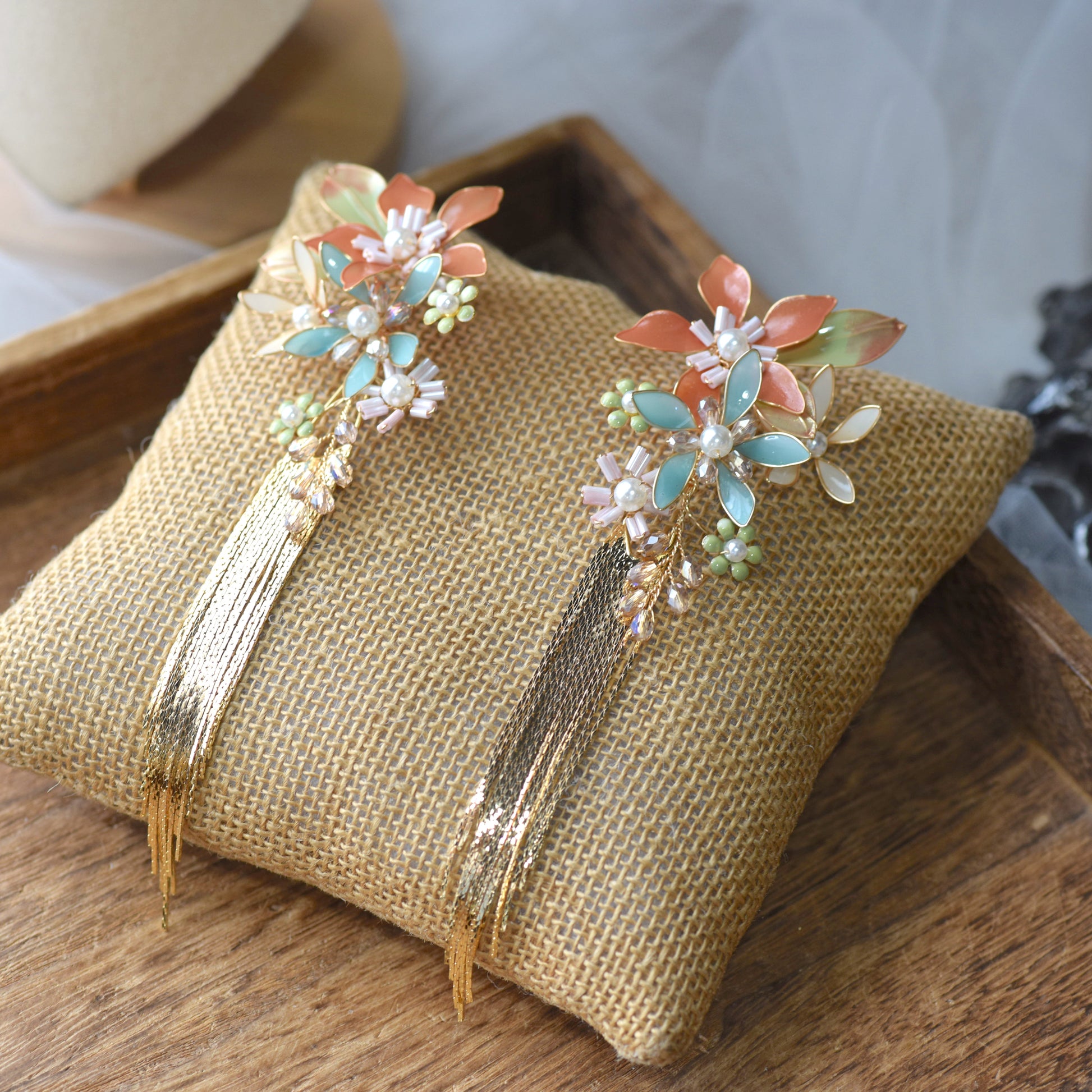 Jeanne coral mint and blue resin floral earrings with golden tassels on a jute cushion
