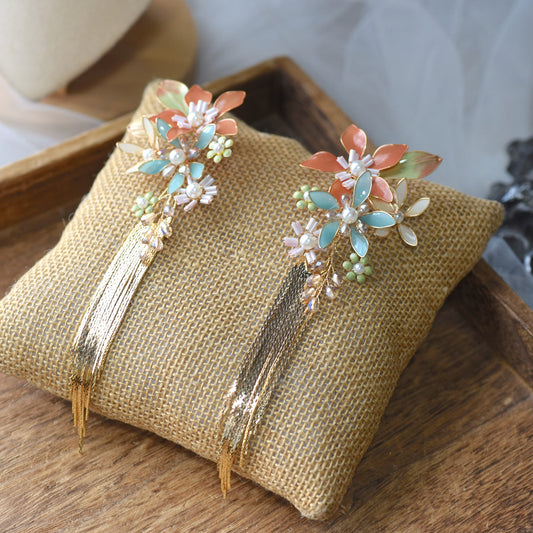 Jeanne coral mint and blue resin floral earrings with golden tassels on a jute cushion
