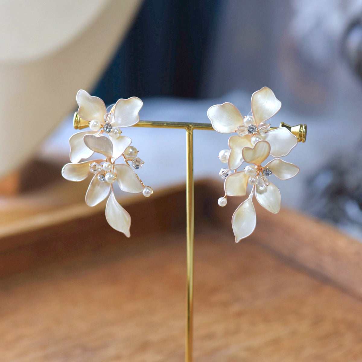 Lunara white resin floral earrings with pearlescent finish and crystal drops on display stand
