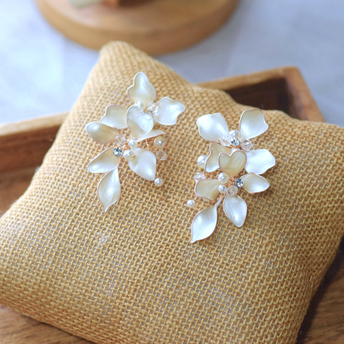 Lunara ivory-white resin floral earrings with pearls on jute cushion
