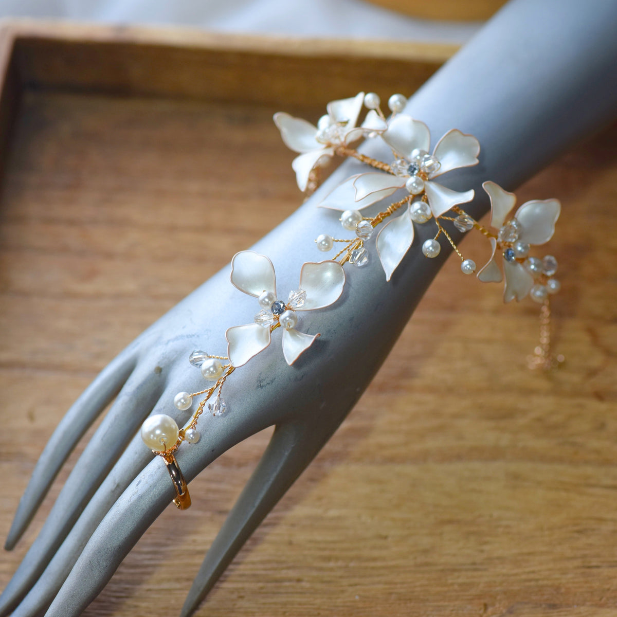 Lunara white and pearl resin floral haath phool with gold chain worn on hand
