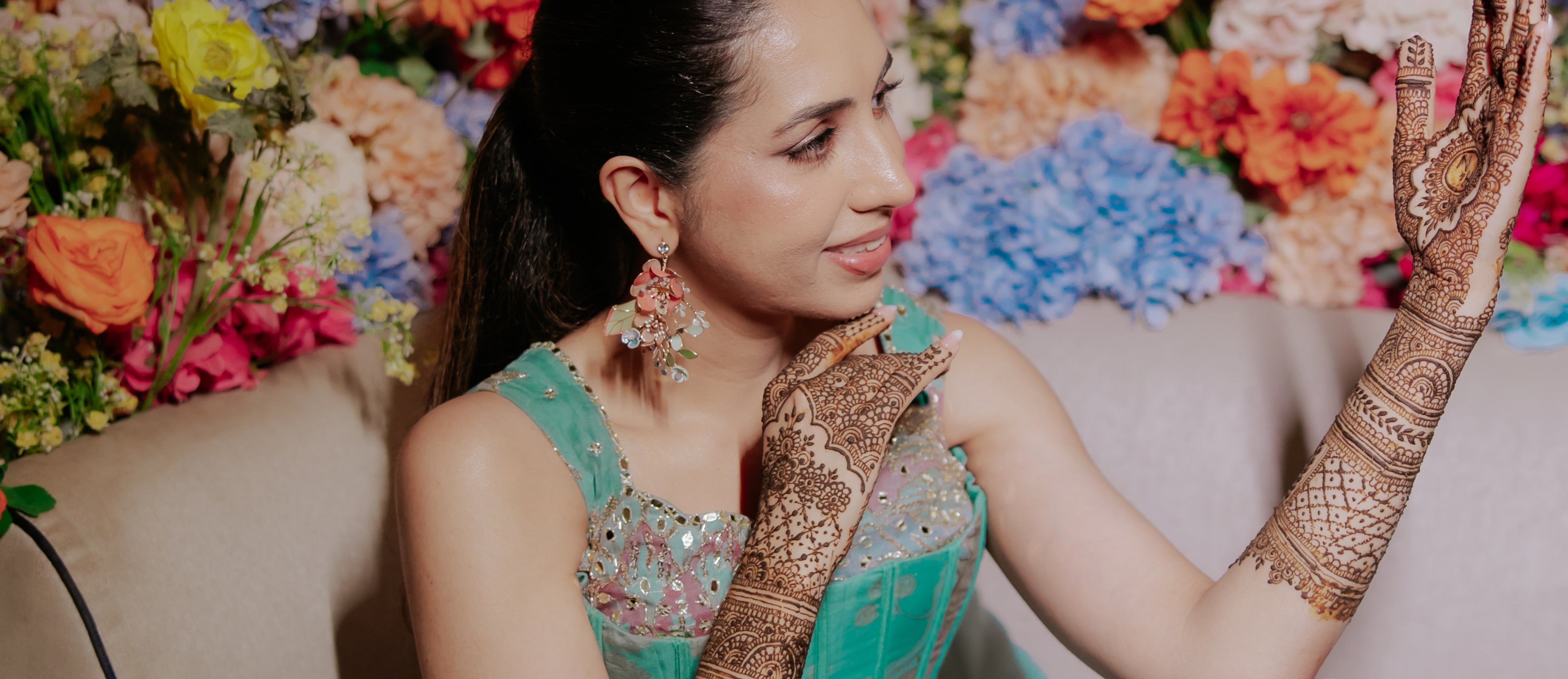 Bride wearing floral mehendi jewellery with henna hands and colorful wedding backdrop