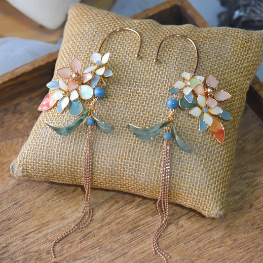 Mehr ivory peach yellow and blue resin floral ear cuffs with teal leaves on a jute cushion

