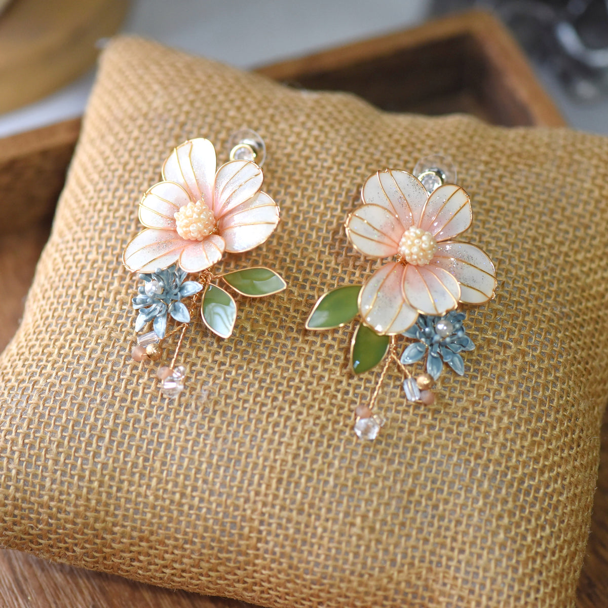 Milla blush peach resin floral earrings with sage green leaves and crystal drop on jute cushion
