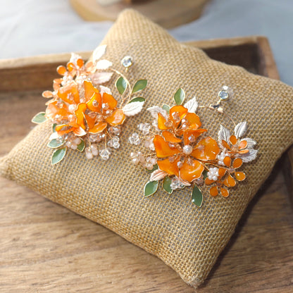 Orelia vivid orange resin floral earrings with green accents and gold leaves on a jute cushion
