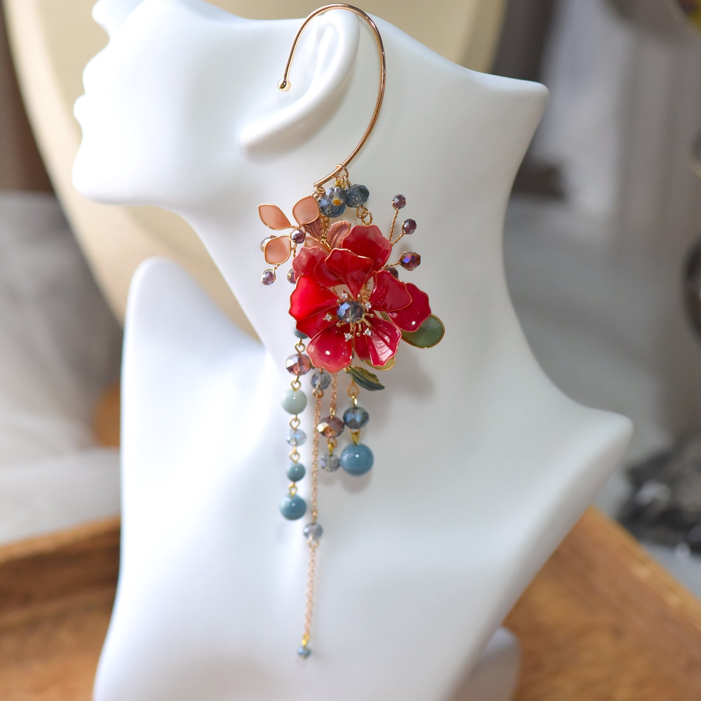 Close-up of Raphael floral ear cuff showing deep red resin petals, crystal bead accents and intricate gold wire finish