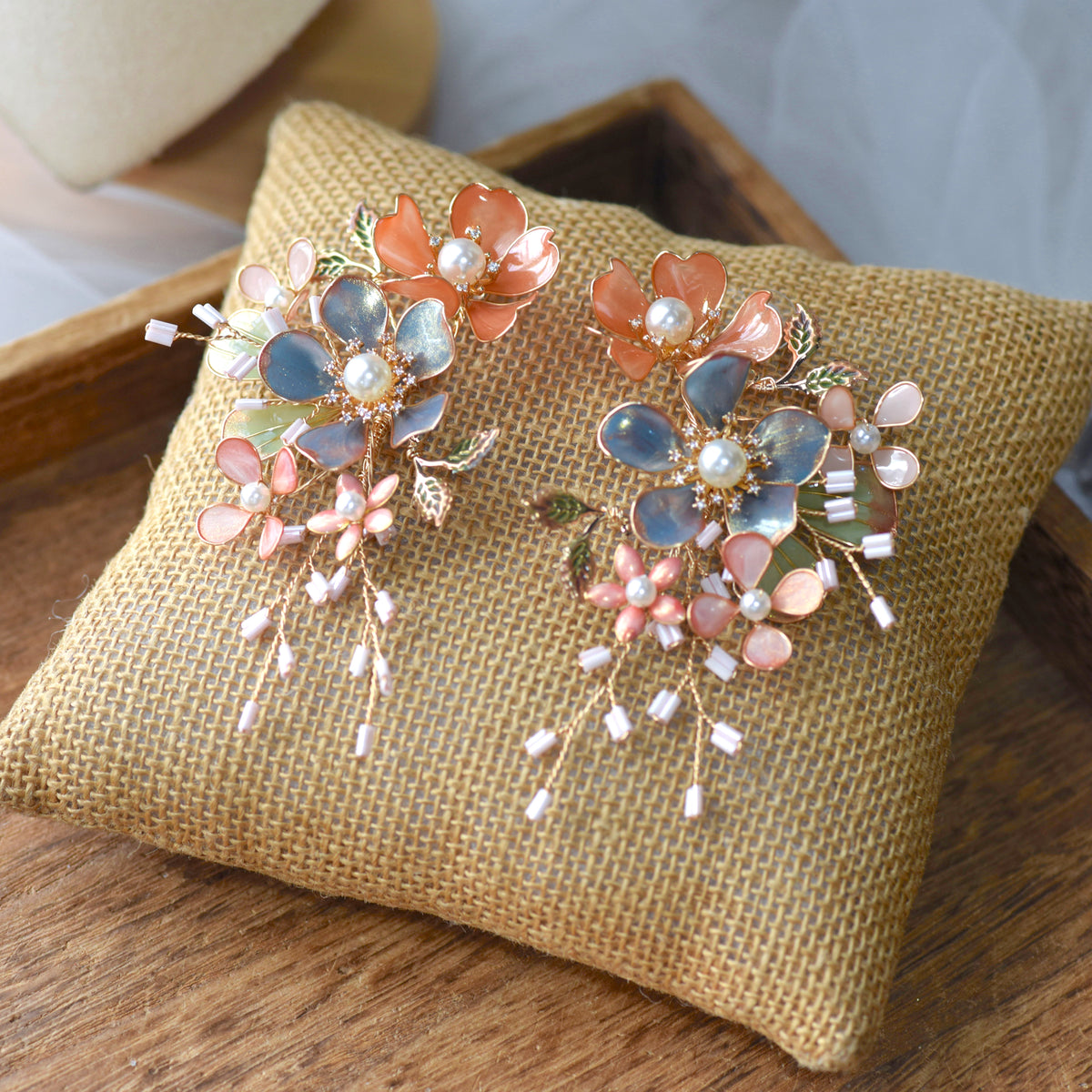 Reine blush pink and dusty blue resin floral earrings with pearl centres on a jute cushion
