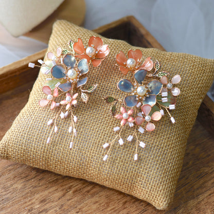 Reine blush pink and dusty blue resin floral earrings with pearl centres on a jute cushion
