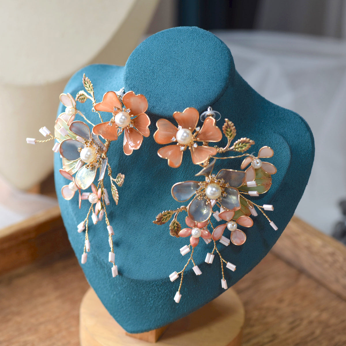 Reine blush and blue resin floral statement earrings displayed on a stand showing beaded sprig detail
