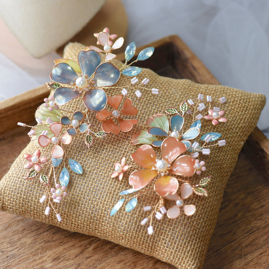 Reine set of two blush pink and dusty blue resin floral hair pins with pearl centres on a jute cushion
