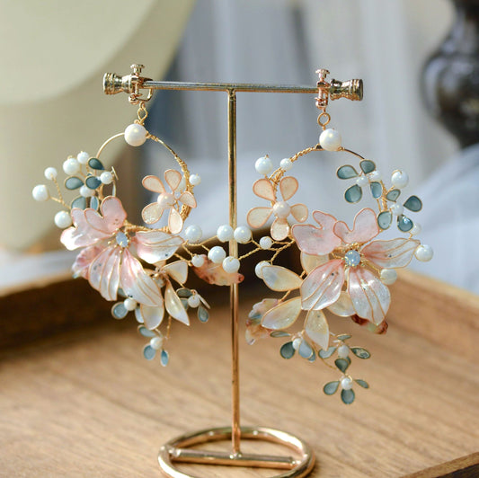 Rivia white and blush pink resin floral hoop earrings with pearls on a display stand
