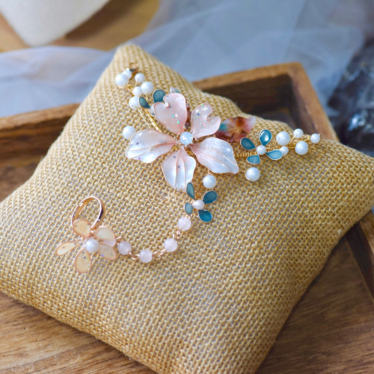 Rivia white and powder pink resin floral haath phool with pearl chains on a jute cushion
