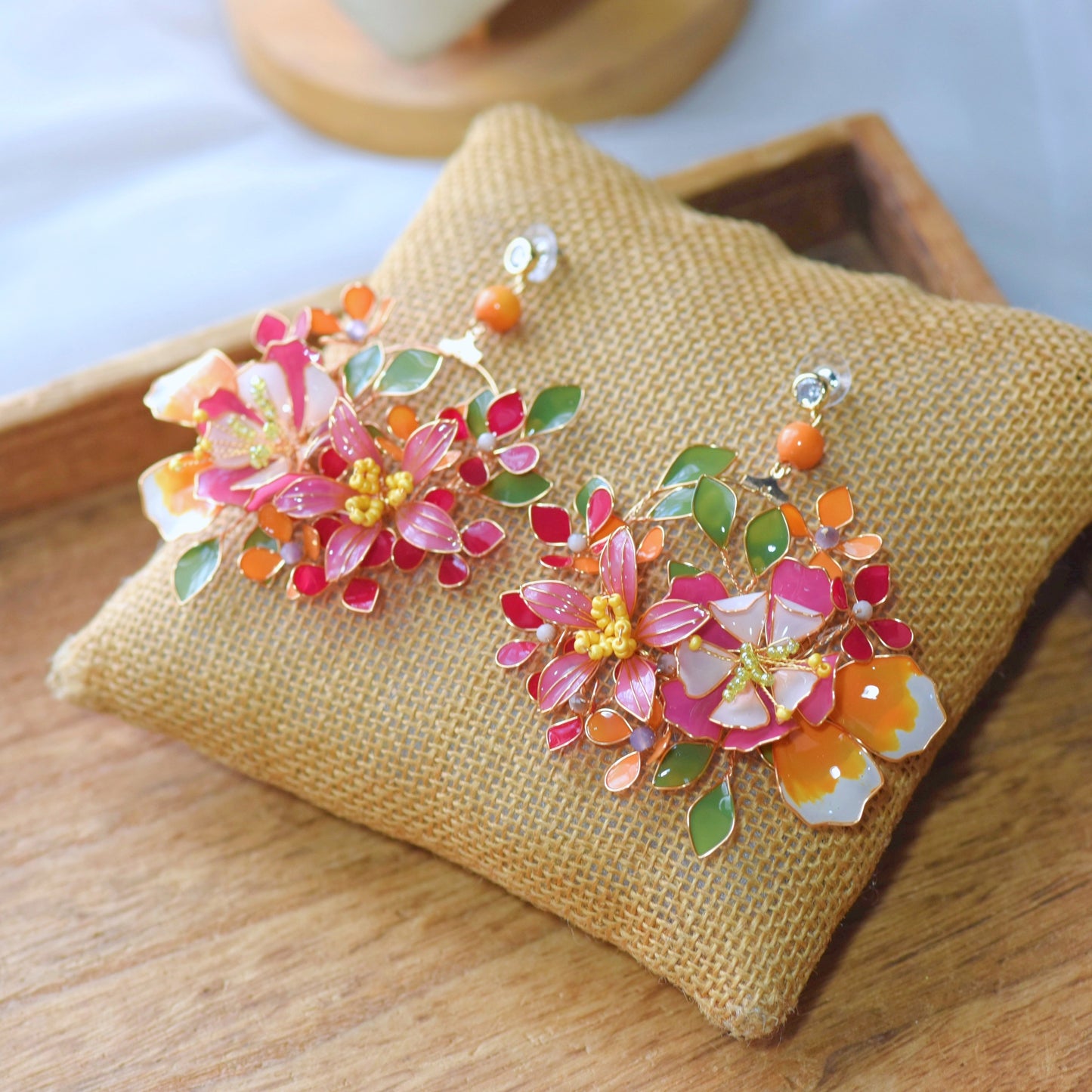 Samara handcrafted resin floral earrings vibrant pink coral orange green gold flat lay burlap cushion