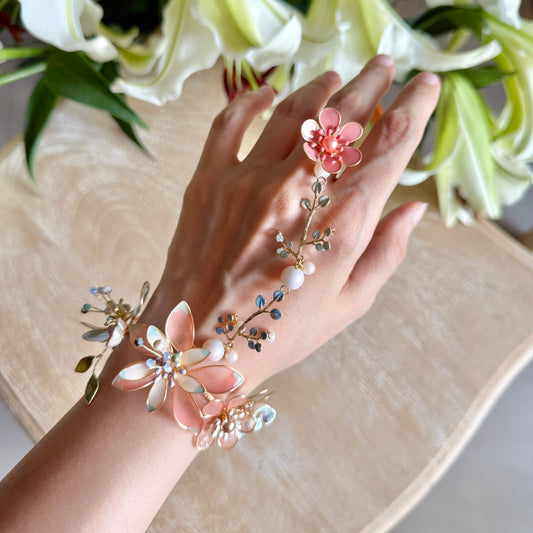 Trina coral and green resin floral hand harness worn on the hand, showing the wrist cluster and finger bloom with lilies behind

