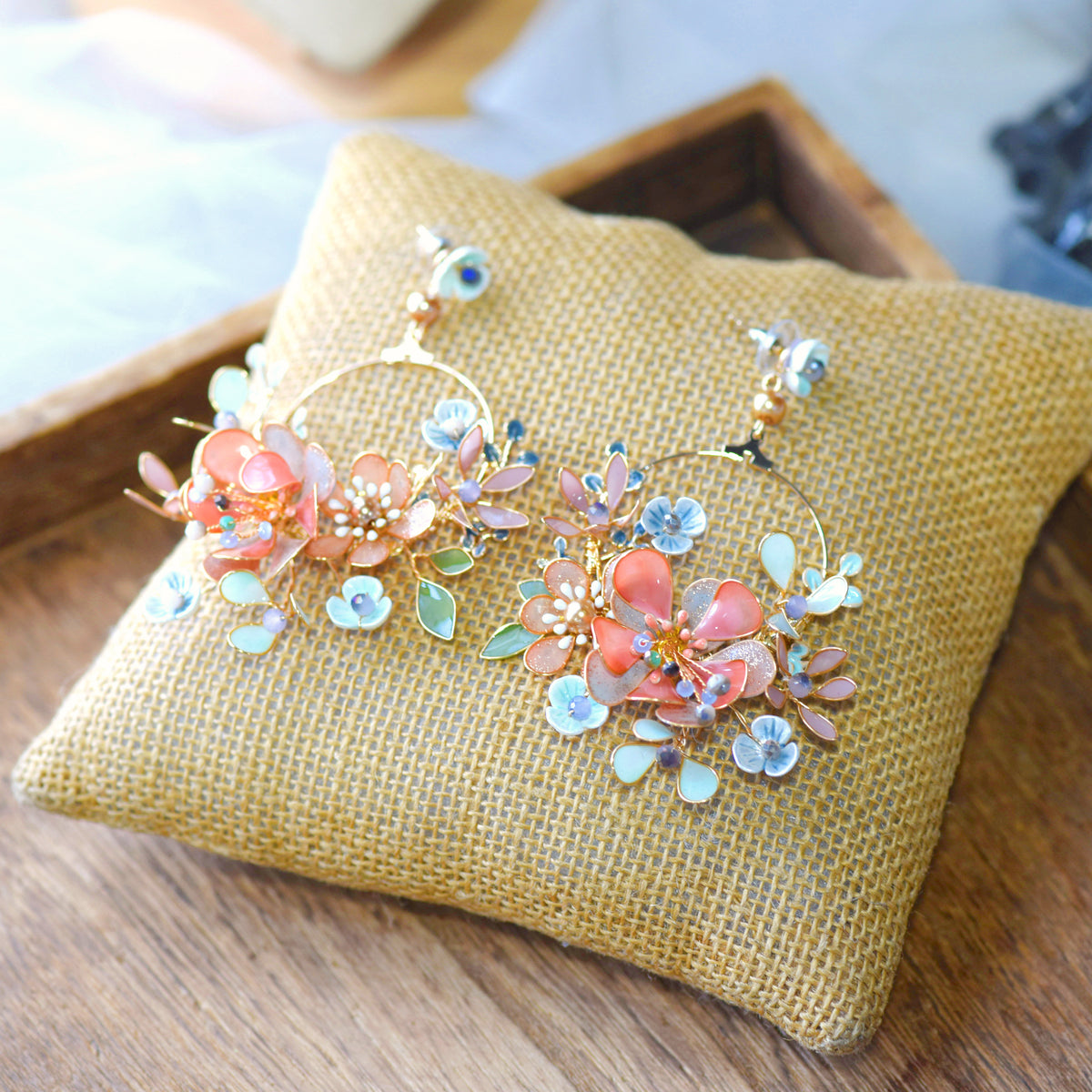 Trina II coral and green resin floral hoop earrings laid on a jute cushion
