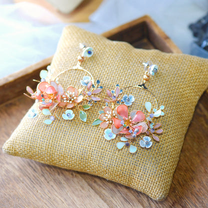 Trina II coral and green resin floral hoop earrings laid on a jute cushion
