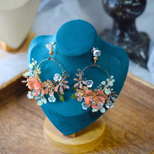 Trina II golden hoop earrings wrapped in coral and green resin florals displayed on a stand
