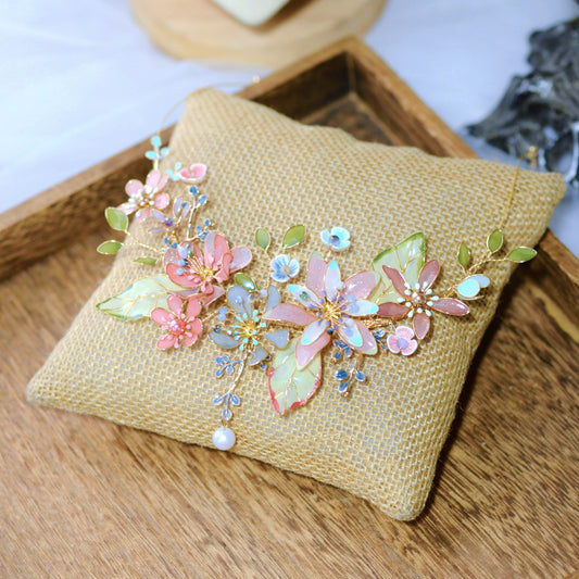 Trina coral and green resin floral necklace with pearl drop laid on a jute cushion
