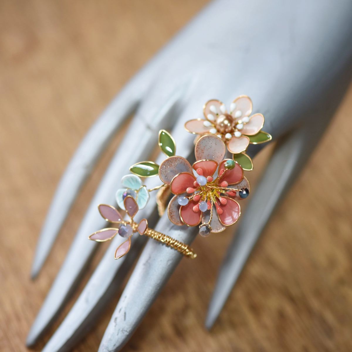 Trina coral and green floral ring on a display hand showing the sculpted bloom and adjustable band

