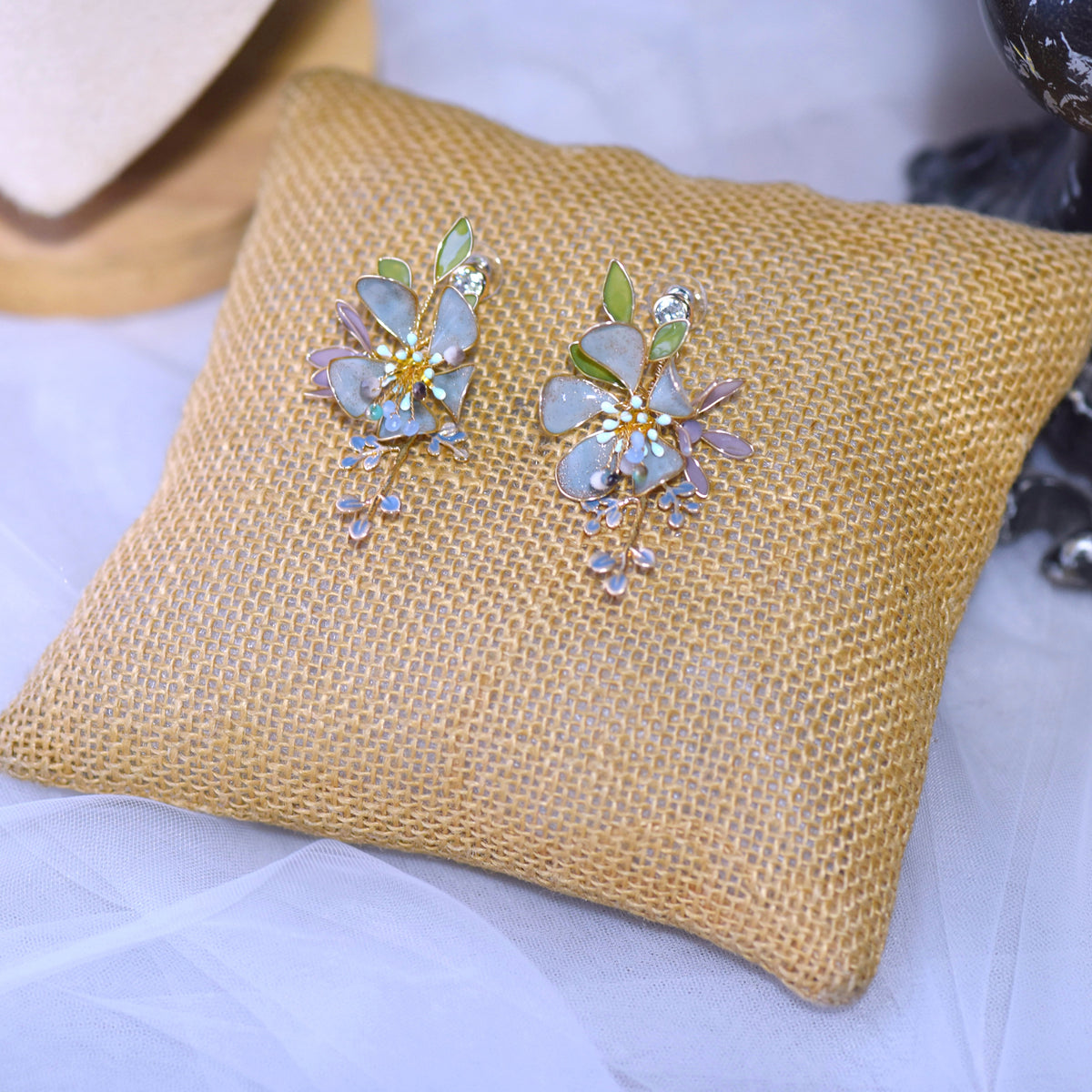 Violet blue and green resin floral earrings laid on a jute cushion
