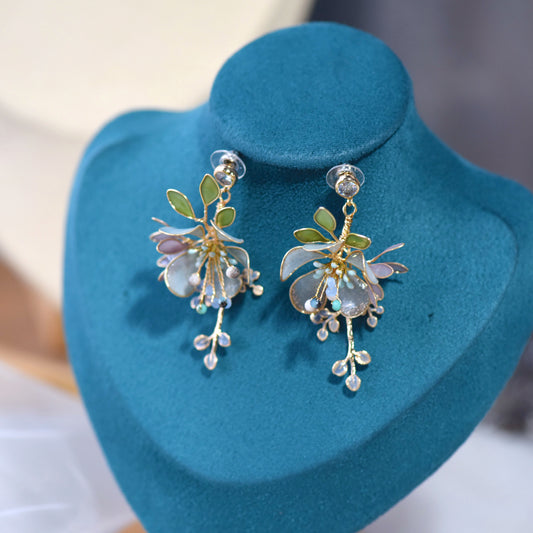 Violet pale blue resin floral earrings with green leaves and beaded drops on a display stand
